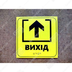 Тактильна табличка Вихід жовтого кольору з пластика з контрастною піктограмою та шрифтом Брайля - фото біля дверей.