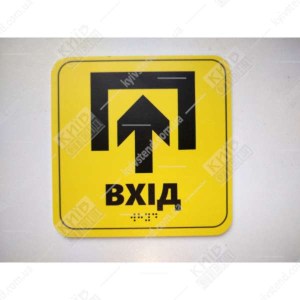 Фото на дверях - тактильна табличка Вхід жовтий пластик з чорною стрілкою та шрифтом Брайля встановлена біля дверей у приміщення.