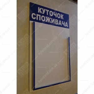 Куточок споживача біло синього кольору з однією обʼємною кишенею з ПВХ пластику, закріплений на стіні у приміщенні для обслуговування клієнтів фото праворуч.
