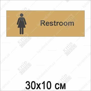 абличка Women з чорним текстом на золотистій пластиковій основі на дверях жіночого туалету у громадському приміщенні