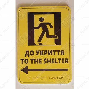 Тактильна табличка to the shelter ліворуч з ПВХ пластику з опуклим шрифтом Брайля встановлена на стіні для навігації до укриття.