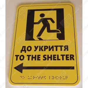 Тактильна табличка to the shelter ліворуч з ПВХ пластику з опуклим шрифтом Брайля встановлена на стіні для навігації до укриття - фото знизу.