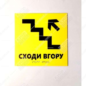 Тактильна табличка жовтого кольору з піктограмою сходів і стрілкою вгору з нанесеним шрифтом Брайля - фото на стіні.