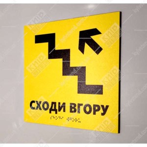 Тактильна табличка жовтого кольору з піктограмою сходів і стрілкою вгору з нанесеним шрифтом Брайля для навігації в будівлі.