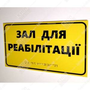 Тактильна табличка з написом Зал для реабілітації жовтий пластик з чорним текстом - фотграфія праворуч на стіні
