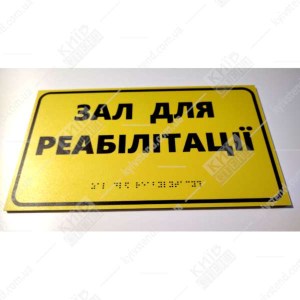 Фото на стіні - тактильна табличка з написом Зал для реабілітації жовтий пластик з чорним текстом встановлена біля входу в приміщення.